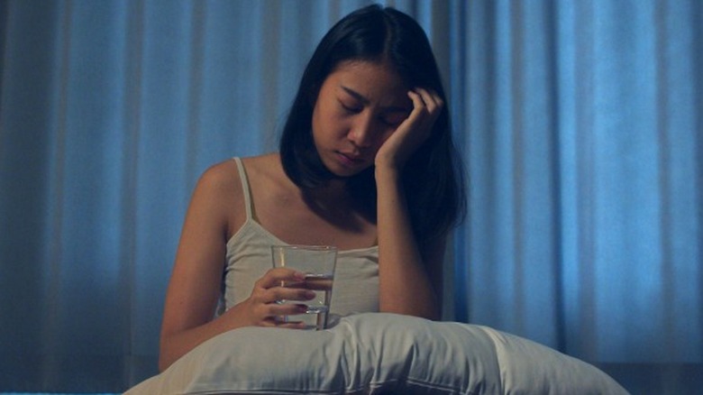 Woman holding cup of water in bed