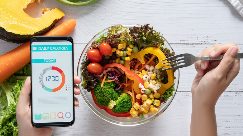 a person using a calorie tracker and eating a salad