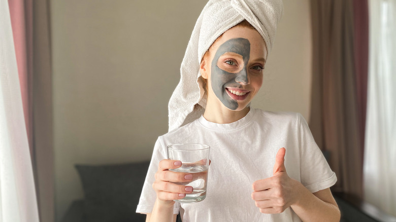 a woman with a clay mask drinking water