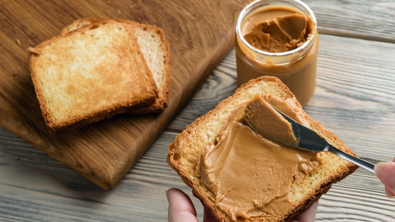 woman's hands spreading peanut butter on bread