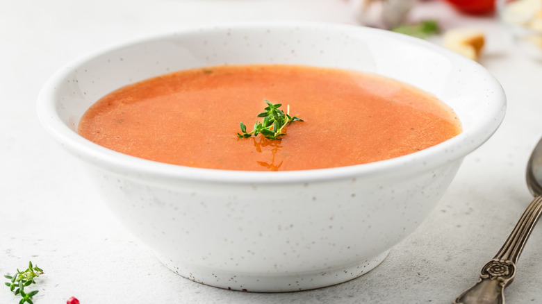 White bowl of creamy tomato basil soup next to a spoon