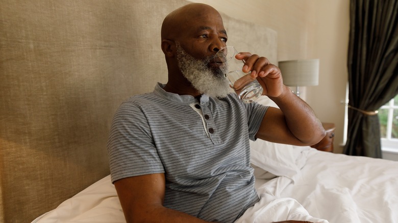 Man drinking glass of water in bed