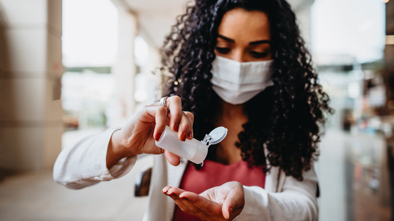 masked woman squeezing out drops of hand sanitizer gel