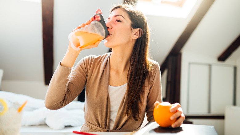 woman drinking orange juice and holding an orange