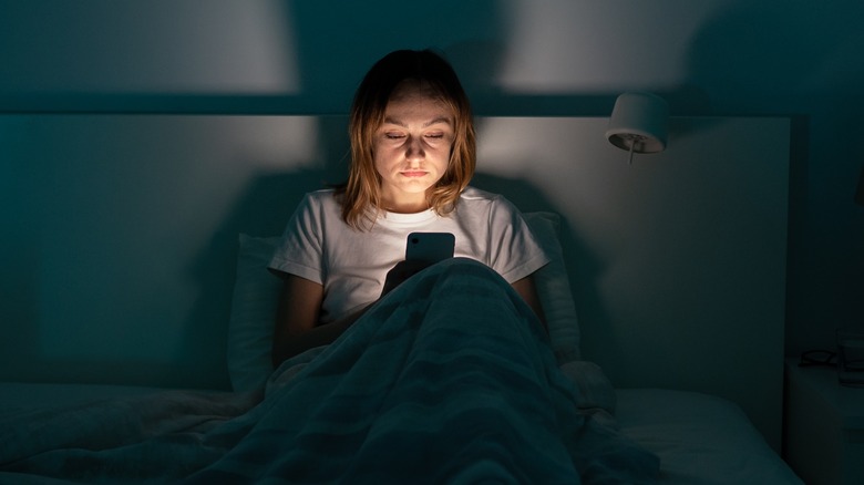 woman sitting up at night in bed scrolling through phone