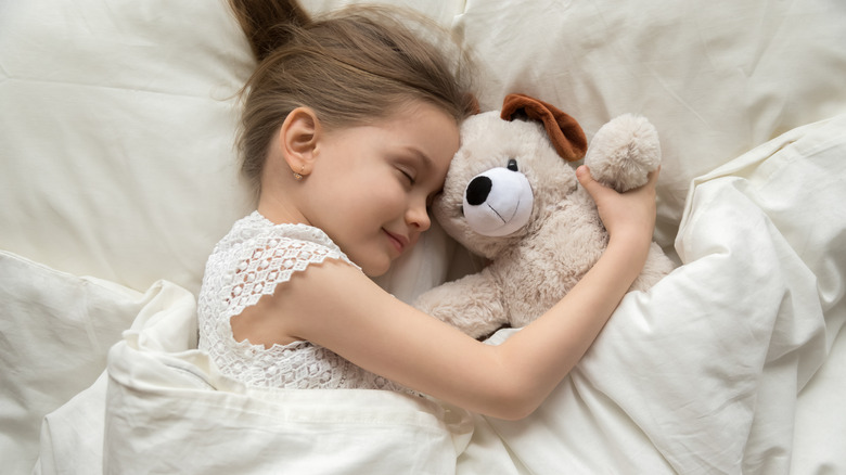 Young girl sleeping in bed cuddling stuffed animal