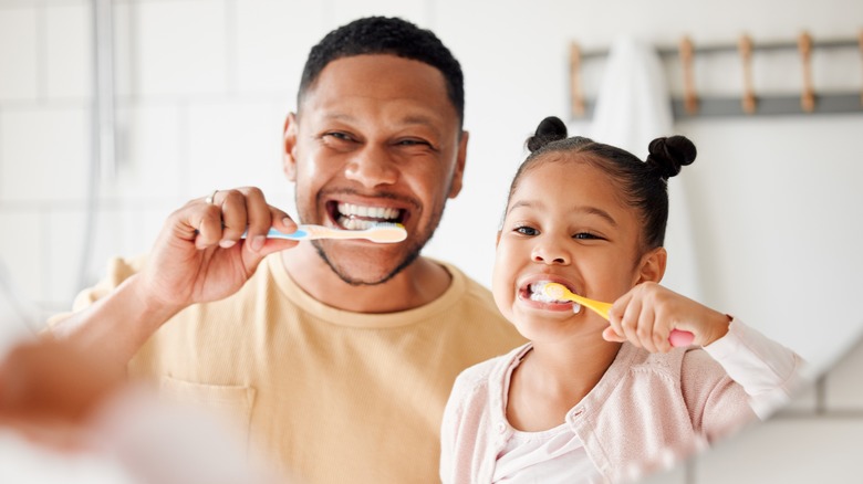 A father and young daughter brushing their teeth