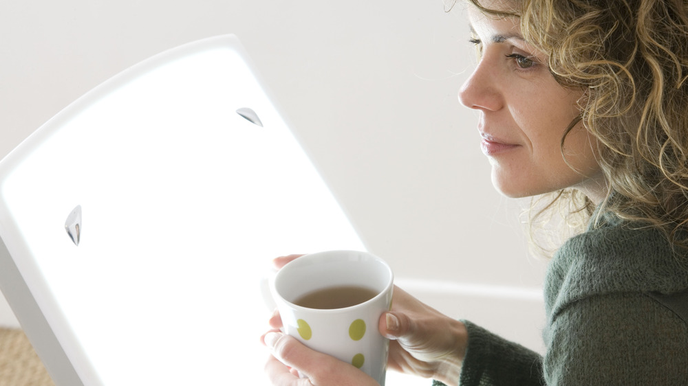 Woman using light therapy with coffee