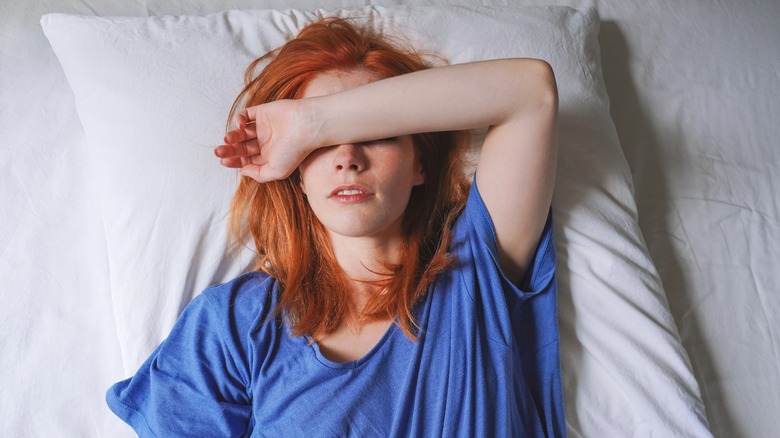 woman in bed using her arm to block light from her eyes