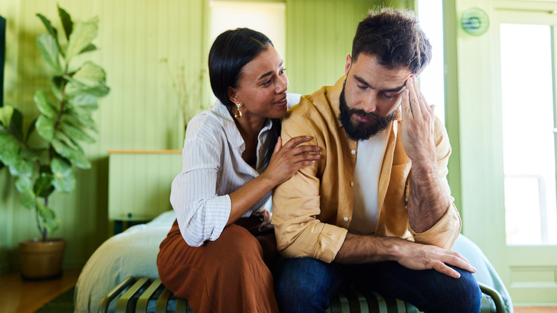 woman sitting on bed comforting man