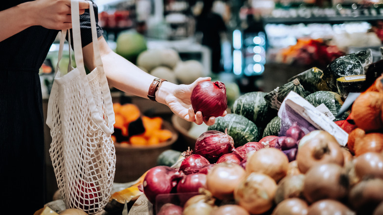 Woman buying fresh onions from a produce display at a grocery store