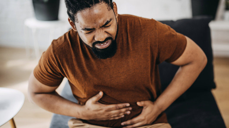 Grimacing man on a couch experiencing stomach pain