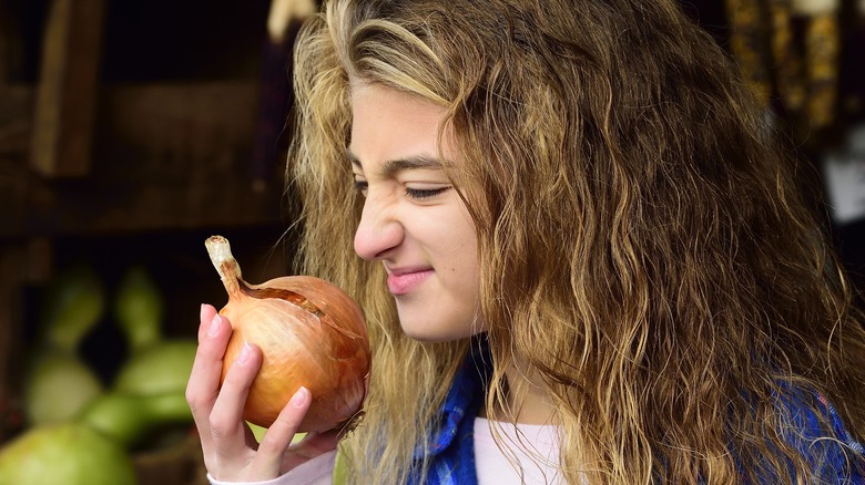 Grimacing woman smelling the unpleasant scent of an onion