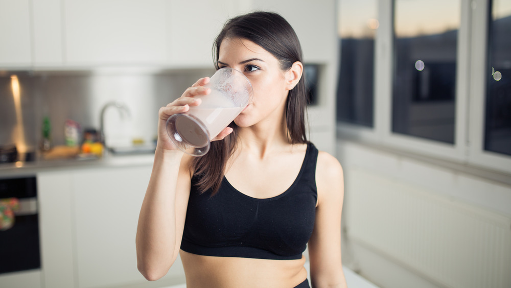 A woman drinks a protein shake in her kitchen