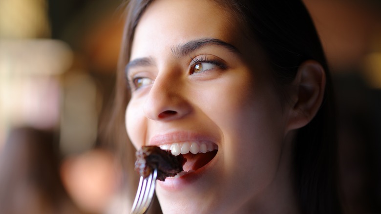 smiling woman eating fork filled with meat in restaurant