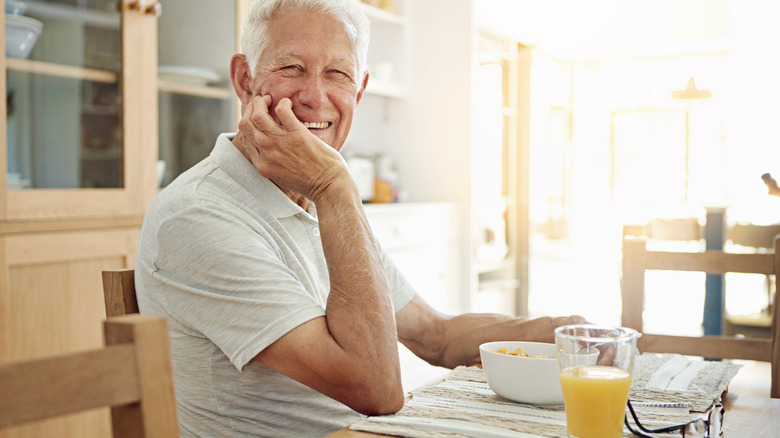 A smiling older man with cereal and orange juice