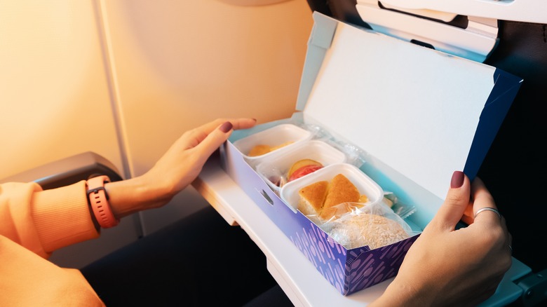 Pair of hands opening a healthy snack box while seated on airplane