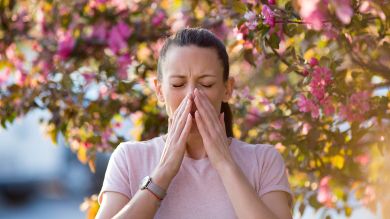 Woman sneezing in front of blooming trees