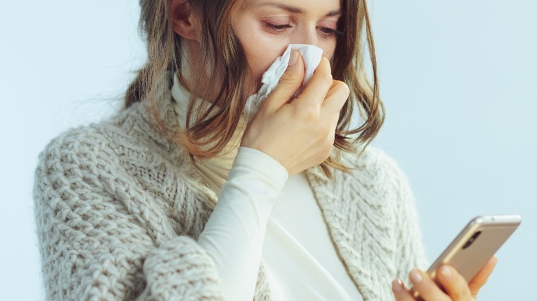 Woman with smartphone wiping nose