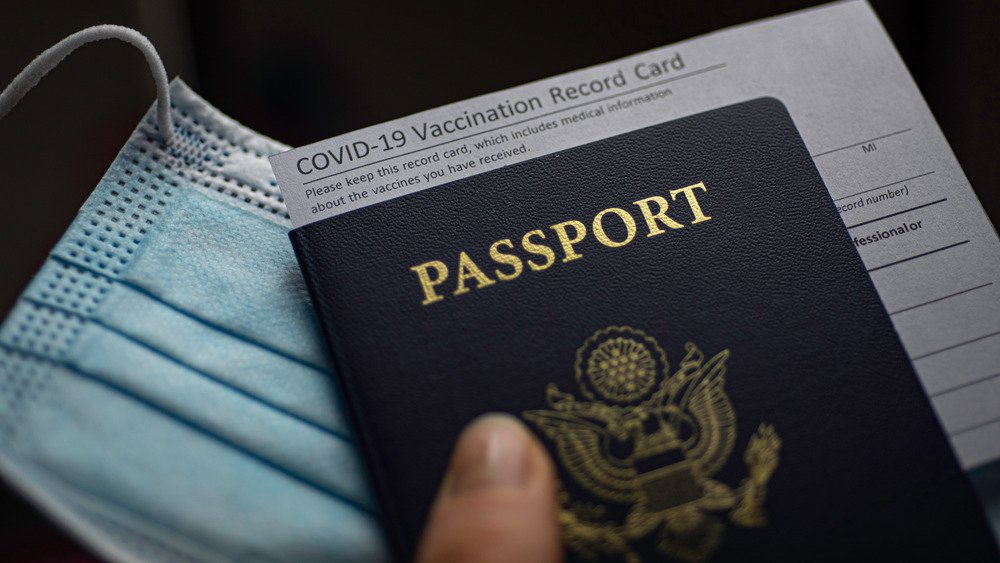 Person holding passport, face mask, and COVID-19 vaccine record