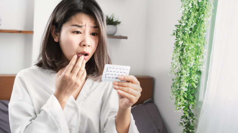 Concerned woman holding birth control pills