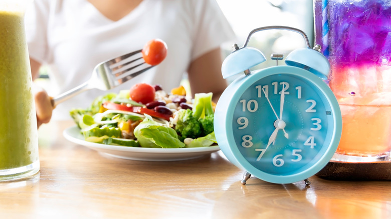 A woman eats in front of a blue clock