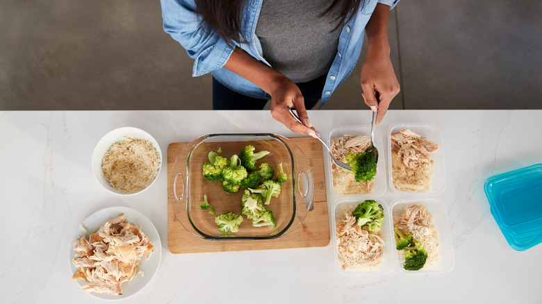 a woman preparing a meal with chicken, broccoli and rice