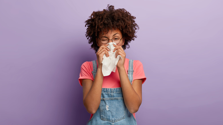 Woman in pink t-shirt and overalls sneezing in a tissue