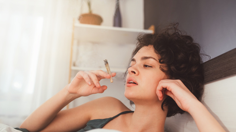 young woman smoking a cannabis joint inside
