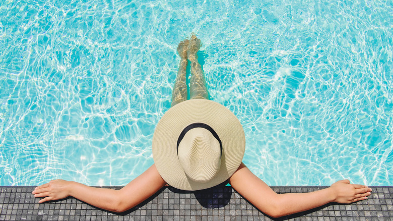 A woman relaxing in a pool at the edge under a large hat
