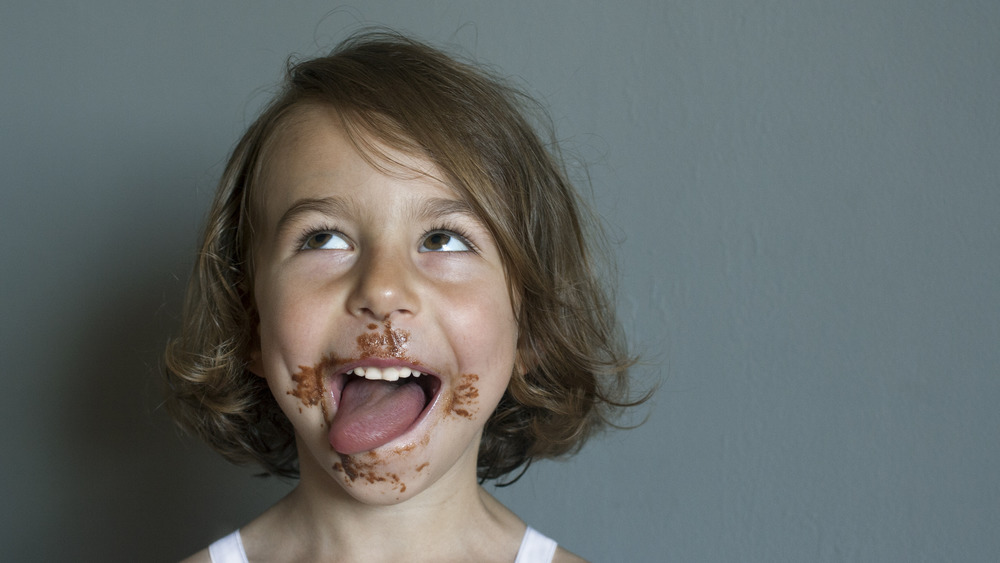 Little girl happily licking chocolate from her face 