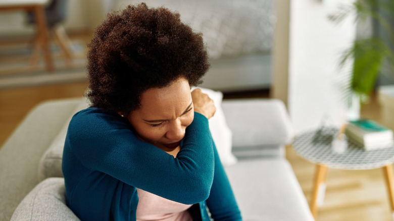 A woman sneezing into her elbow