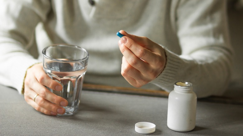 Hands holding pill and water glass