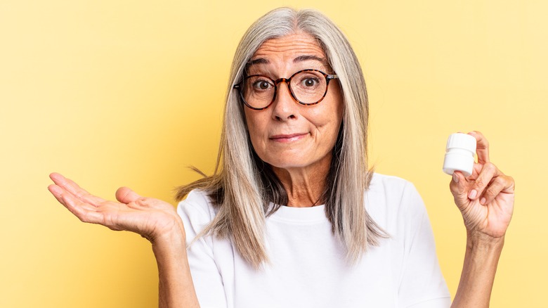 Older woman shrugging holding pills