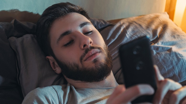 man looking at phone in bed