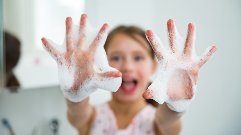 Young girl holding up soapy hands