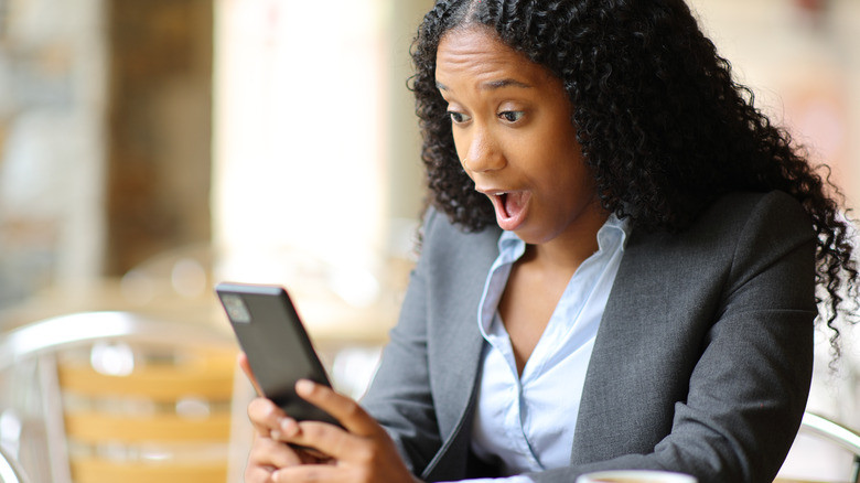 young woman surprised while reading on phone