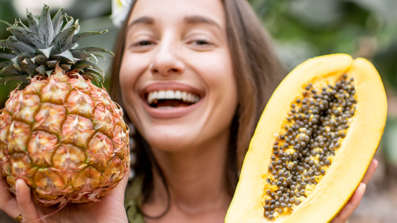 woman holding pineapple and sliced papaya