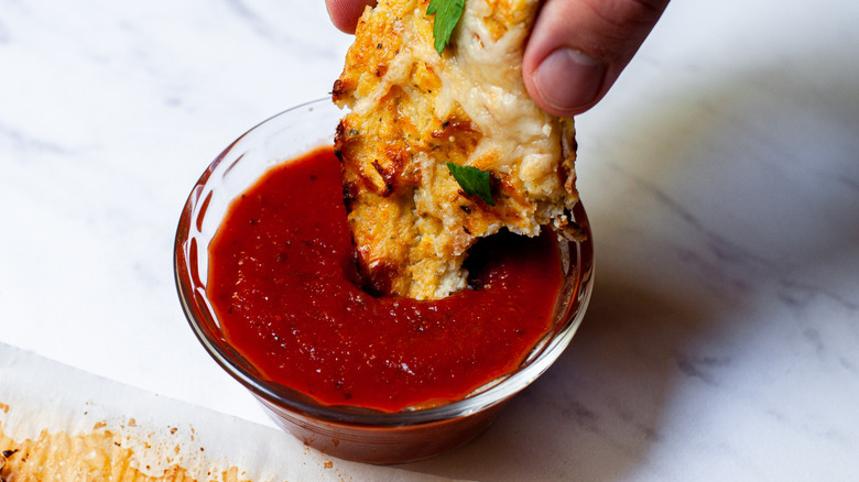 Cheesy caultiflower being dipped into marinara sauce