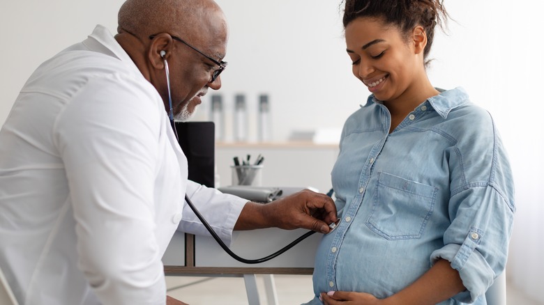 smiling doctor listening to pregnant stomach