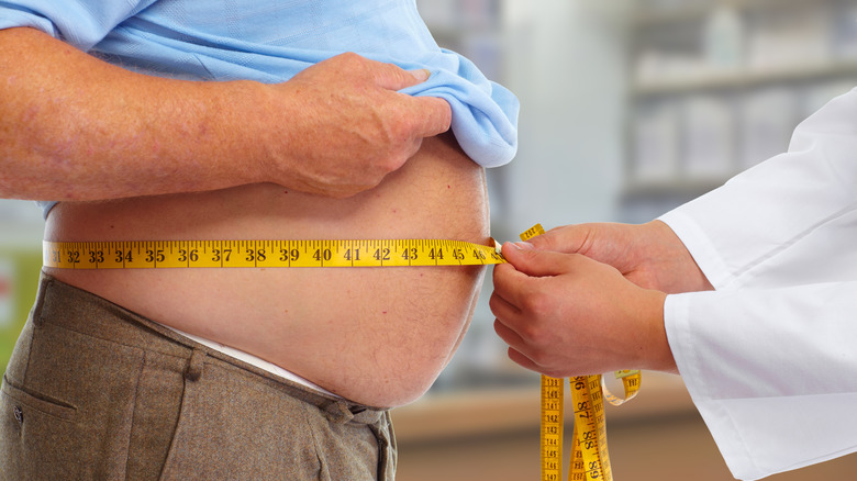 older man with large belly measured by doctor