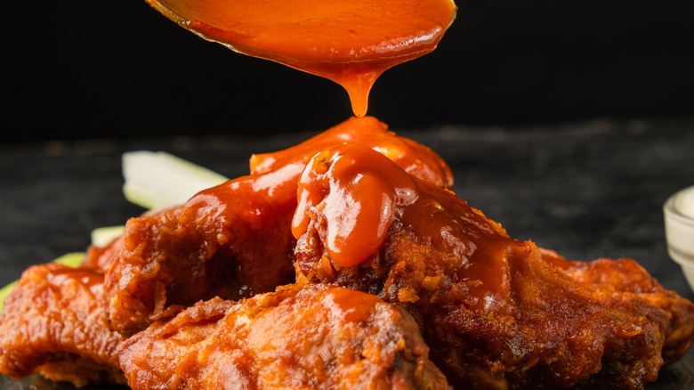 hot sauce being poured over chicken wings