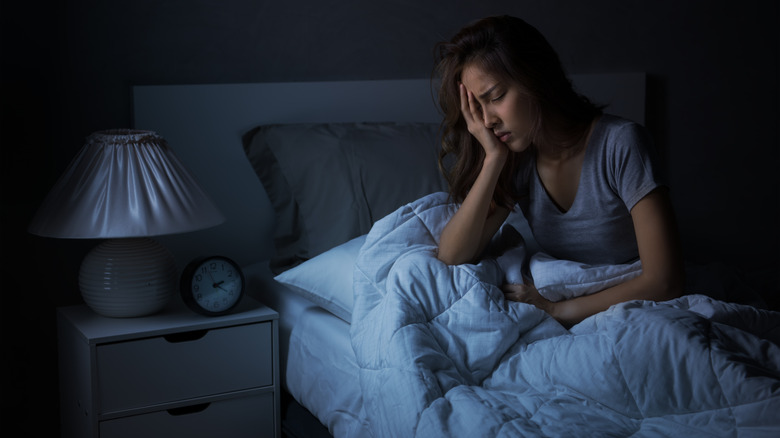 Distressed woman holding her head while sitting up in bed