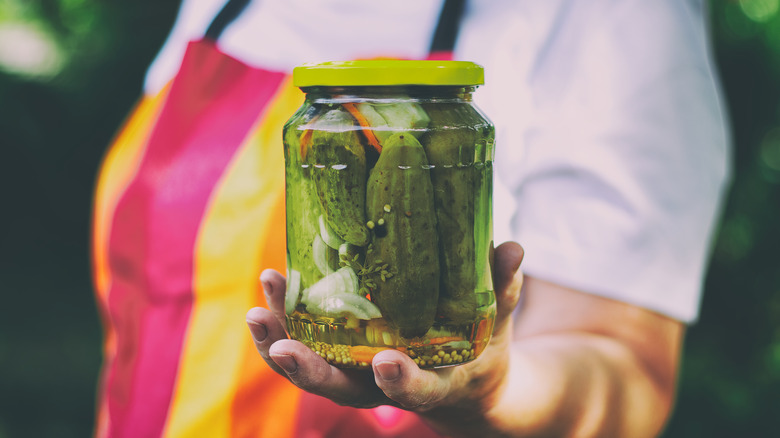 Woman in a colorful apron holding out a jar of pickles