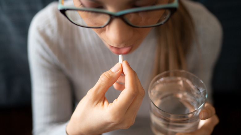 Woman taking tablet with glass of water