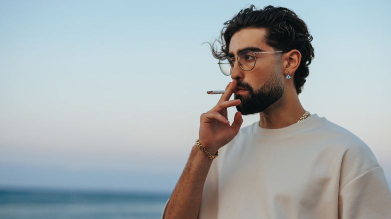 Man standing on a beach smoking a cigarette