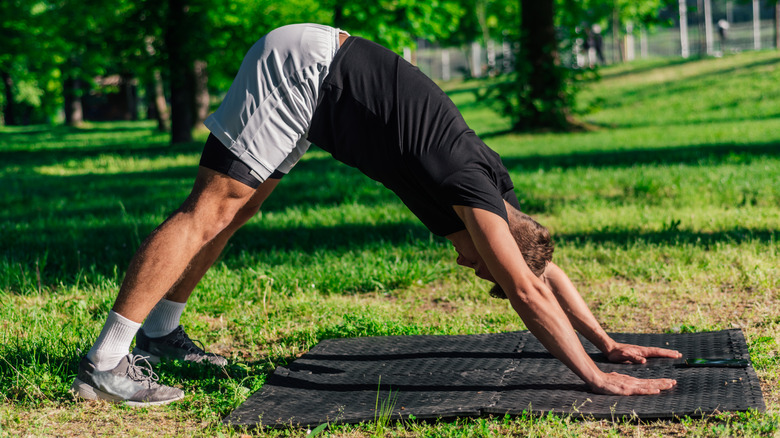 man doing downward-facing dog yoga pose outdoors