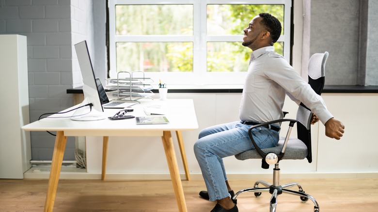 Man stretching arms seated at desk