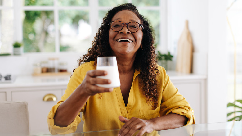 older woman smiling in her kitchen while holding a glass of milk