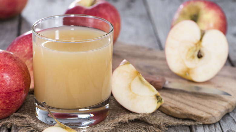 A glass of cloudy apple juice next to several apples and sliced apples